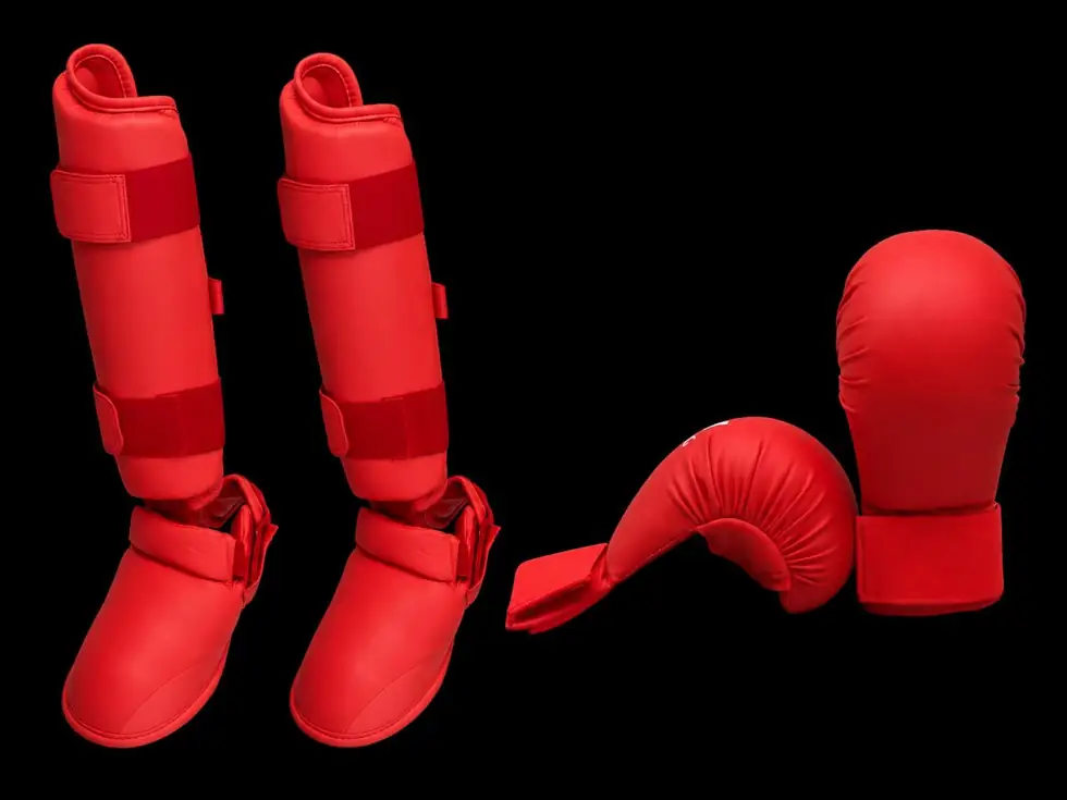 Red karate sparring gloves and shin pads on a black background