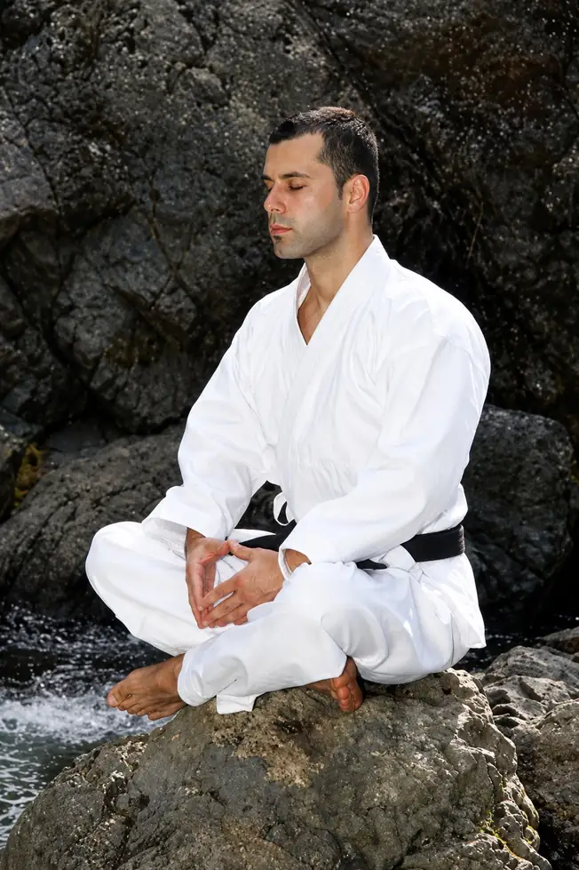 WTMA martial artist meditating in a white gi on rocks